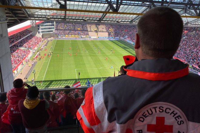 Foto: Mitarbeiter des DRK-Sanitätsdienstes blicken auf das Spielfeld im Stadion.